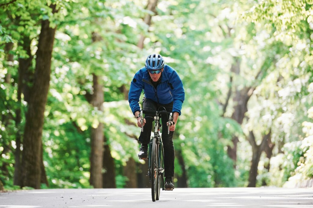 Stamina and strength. Cyclist on a bike is on the asphalt road in the forest at sunny day